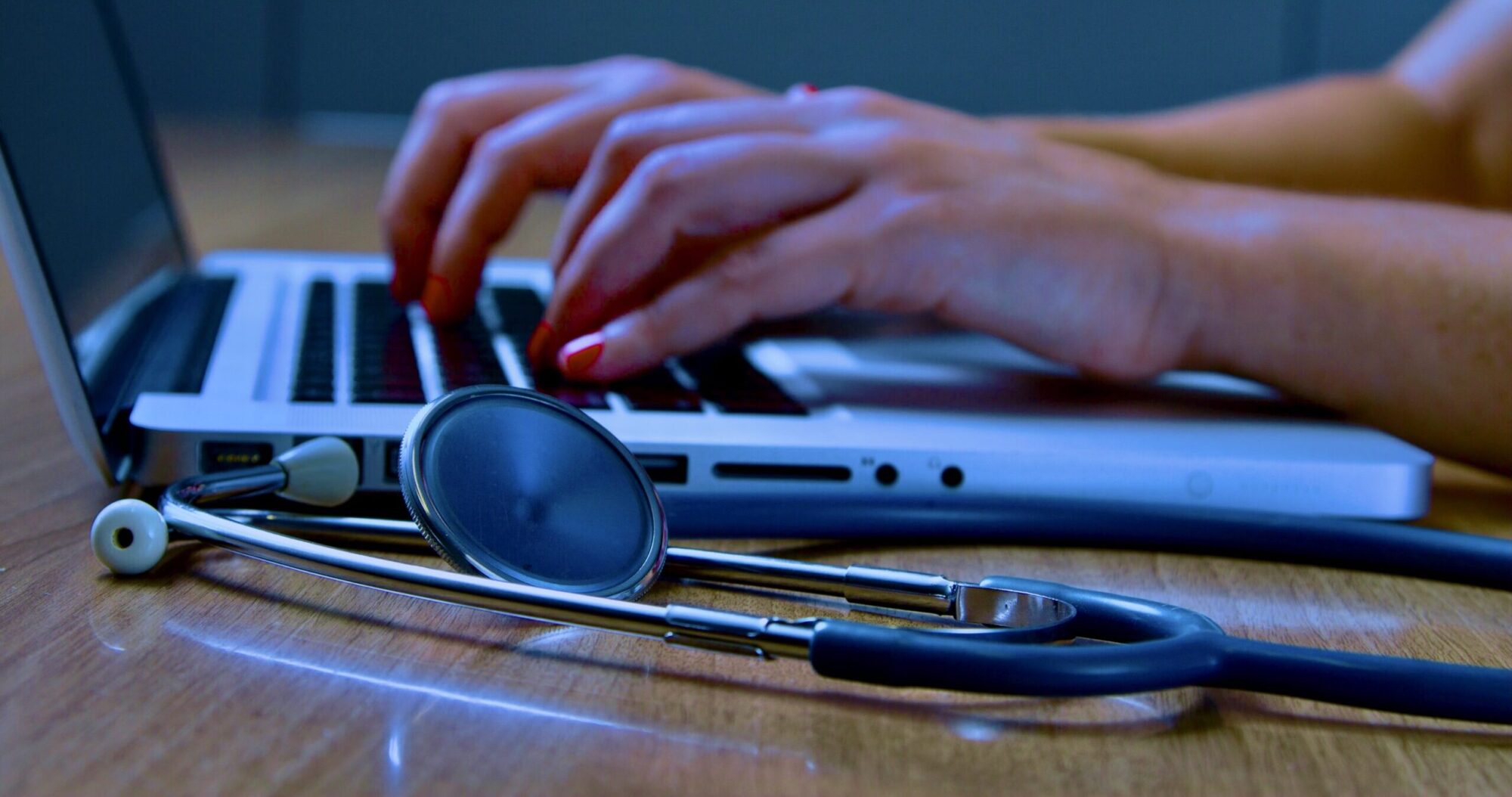 Women's hands typing on laptop with stethoscope in foreground